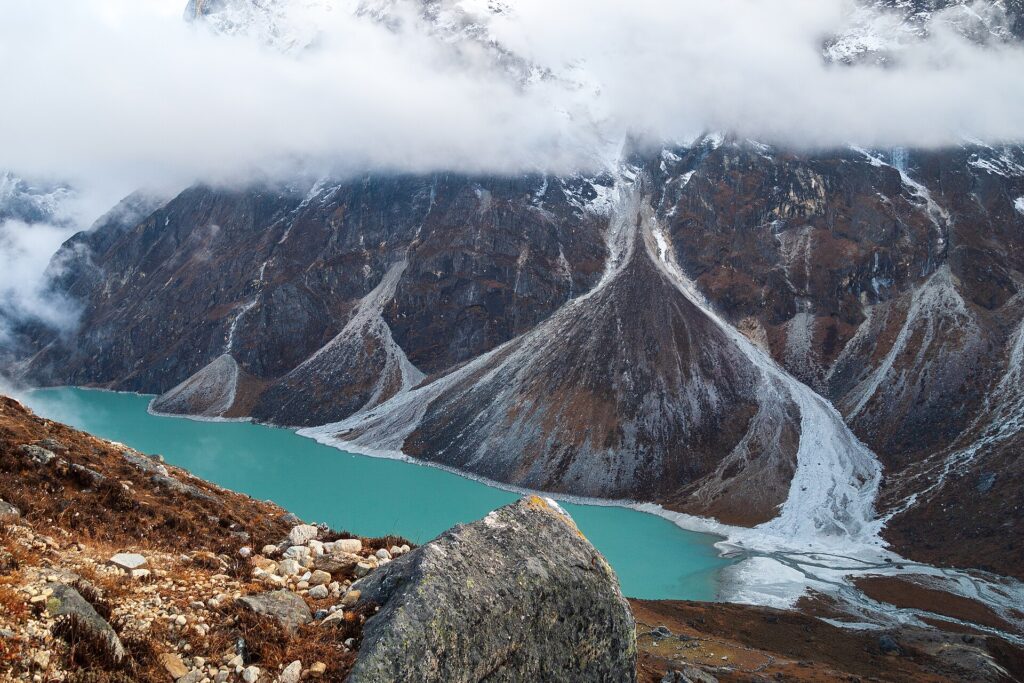 Dunkler Karsee unter steilen Felsw&auml;nden, umgeben von Nadelwald und braunem Grashang