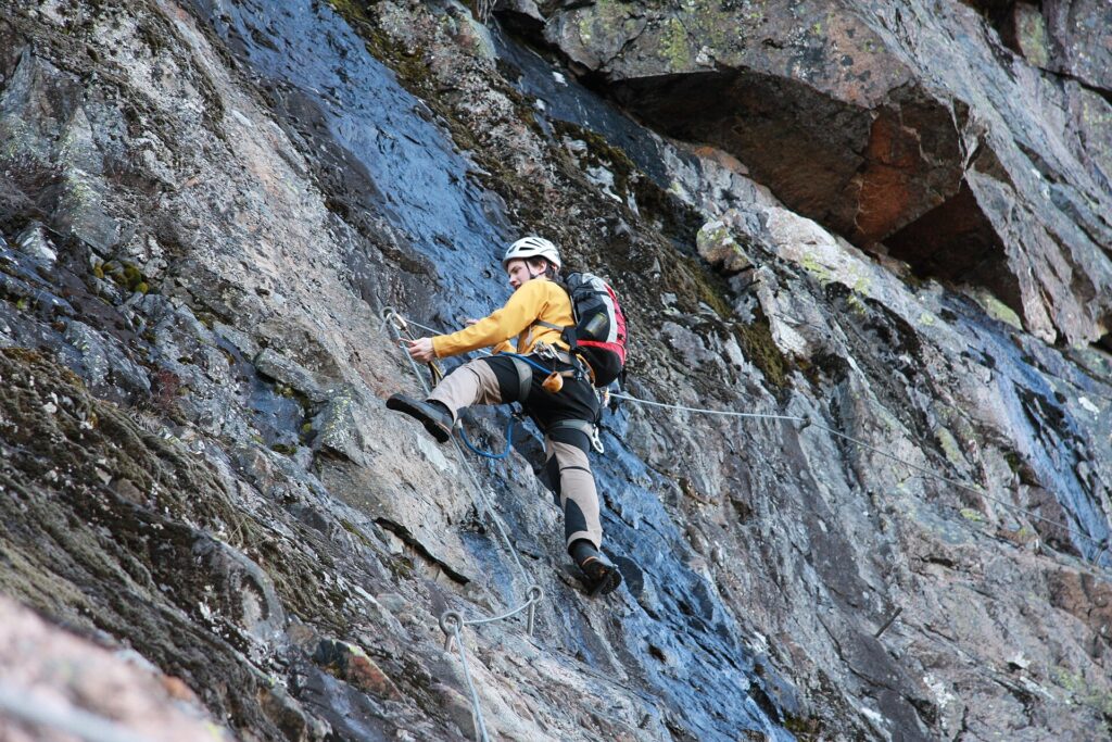 Stahlseil, Trittstifte und ein Klettersteigset an einer senkrechten Felsstufe im Schatten