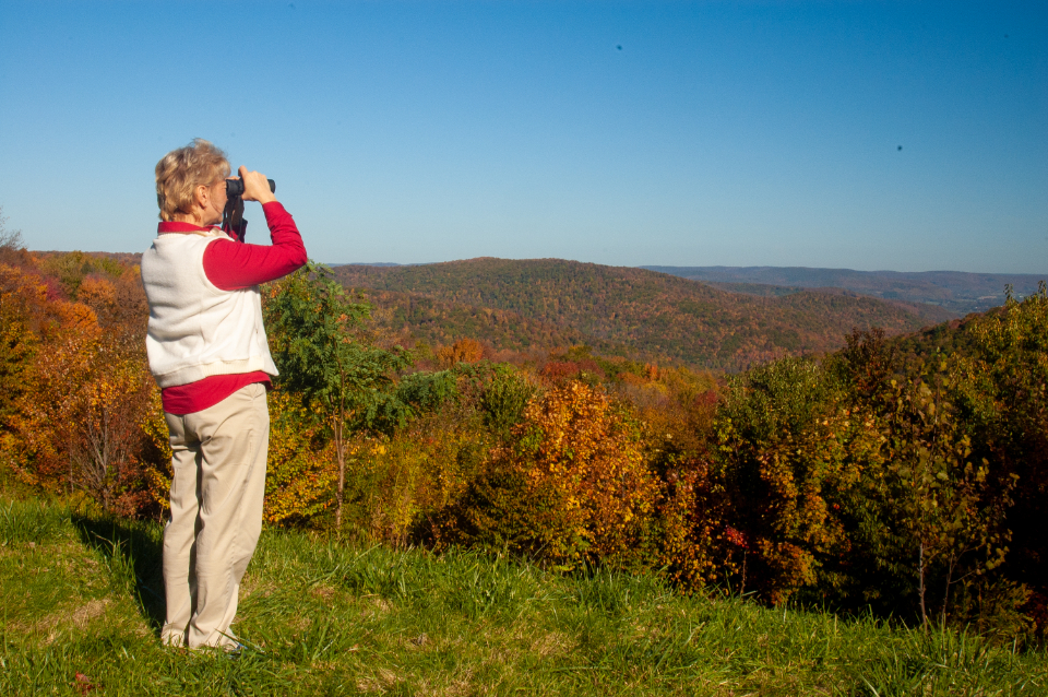 Fernglas in beiden H&auml;nden, im Hintergrund offene Landschaft mit tief stehender Herbstsonne