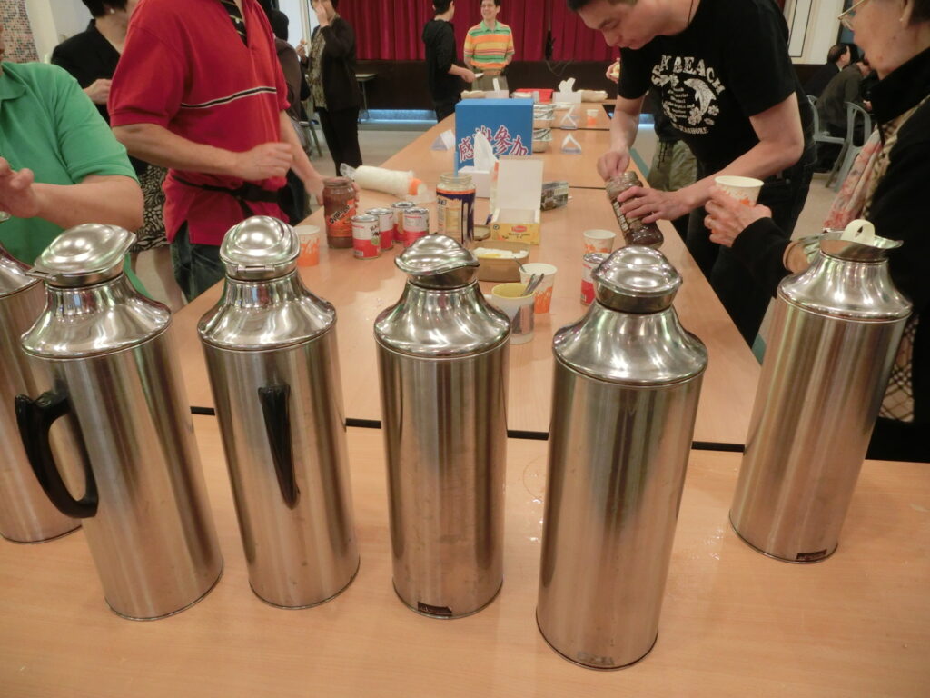 Isolierflasche und dampfender Becher auf einem Stein, dahinter kaltes Bergpanorama
