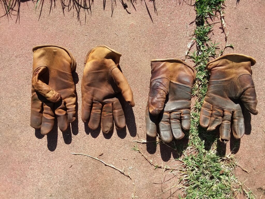 Handschuhe hängen mit der Stulpe nach unten an einer Leine in einem hölzernen Trockenraum