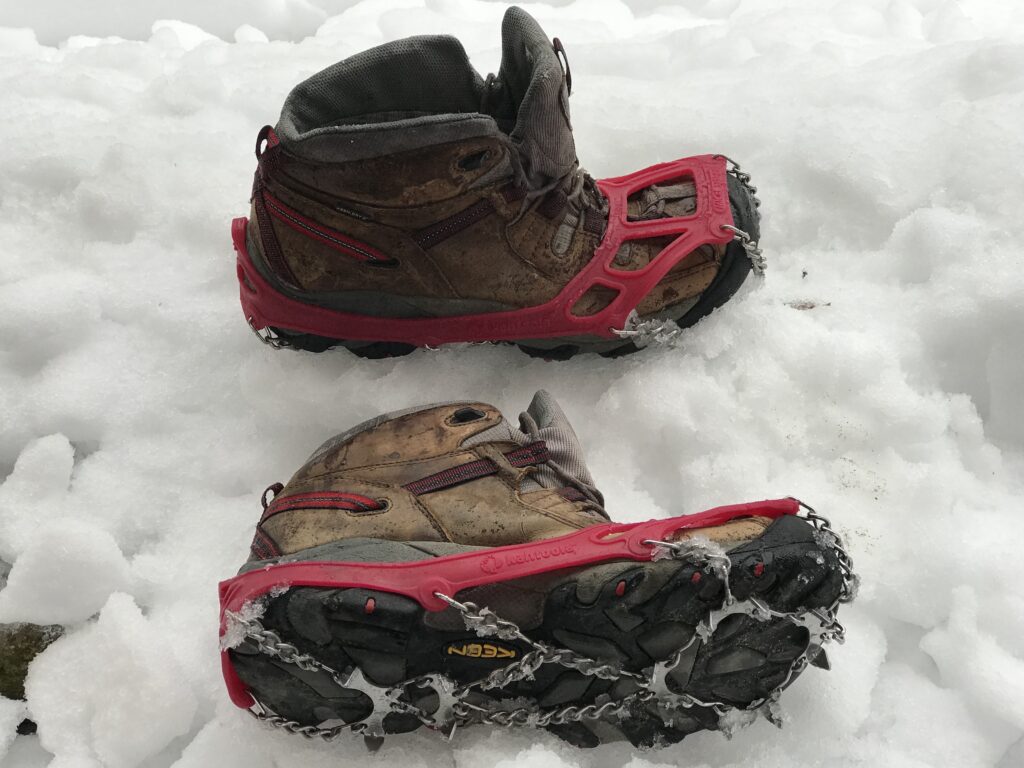 Gr&ouml;del mit kurzen Zacken &uuml;ber einem Wanderschuh auf einem gefrorenen Waldweg