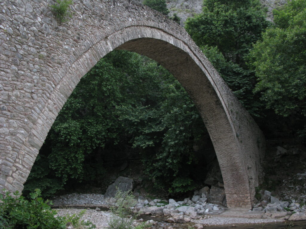 Doppelbogige Steinbrücke über einem klaren Bergfluss zwischen hellen, glatt geschliffenen Felsen