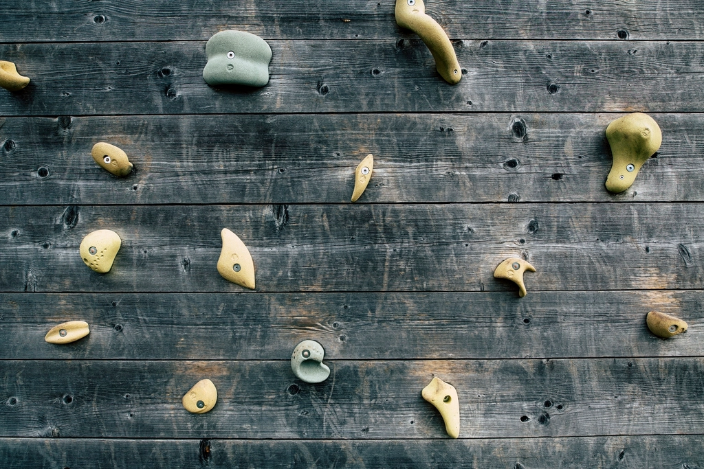 Boulderer im &Uuml;berhang mit gestreckten Armen, unter der Wand liegen dicke Matten